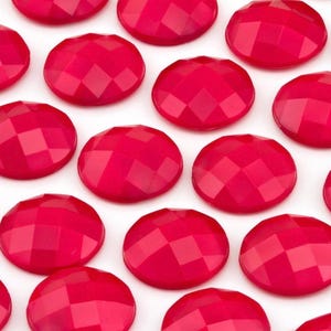 May include: A collection of round, hot pink cabochons arranged in a grid pattern. Each circular piece features a faceted top surface with a geometric diamond-cut design that reflects light, creating a uniform appearance across all the items.