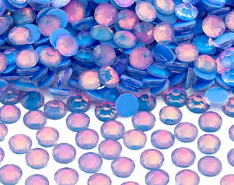 May include: A pile of iridescent blue and pink round glass rhinestones. The rhinestones are scattered on a white surface.