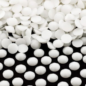 May include: White round flat-back rhinestones, some are scattered on a black surface, while others are piled up in a heap.