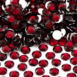 May include: A large pile of red, round, flat-backed rhinestones. The rhinestones are scattered on a white surface.