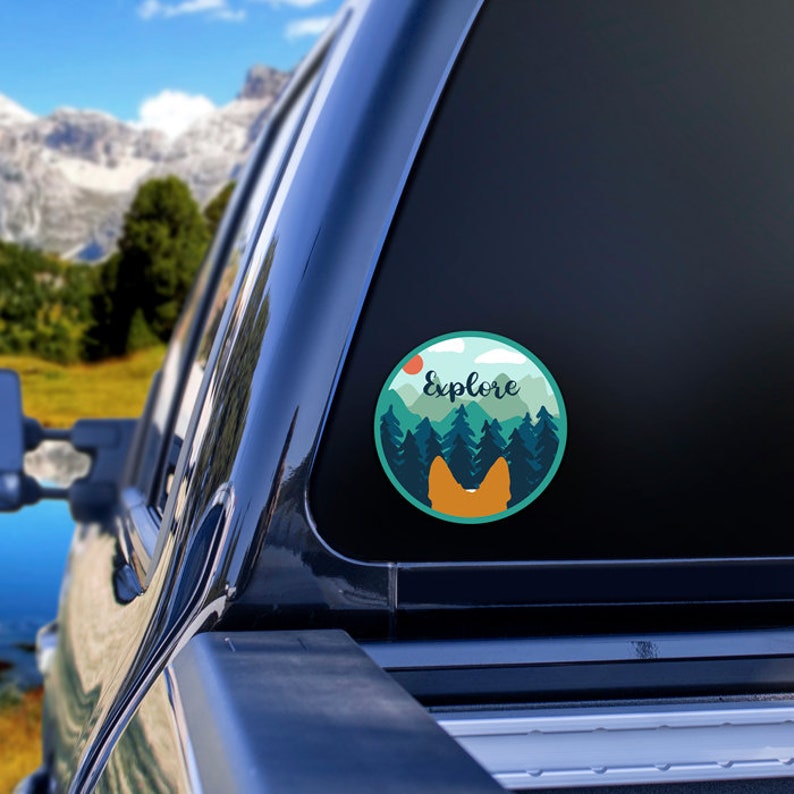 May include: A round sticker with a mountain scene, a red sun, and the word "Explore" in white text. A silhouette of a dog's rear end is in the foreground.