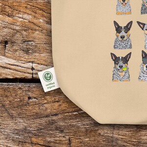 May include: A beige tote bag with a pattern of Australian Shepherd dogs in various poses. The bag has a green label that says "certified organic".