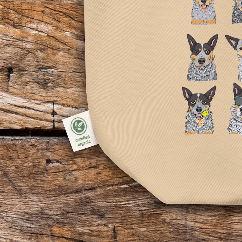 May include: A beige tote bag with a pattern of Australian Shepherd dogs in various poses. The bag has a green label that says "certified organic".