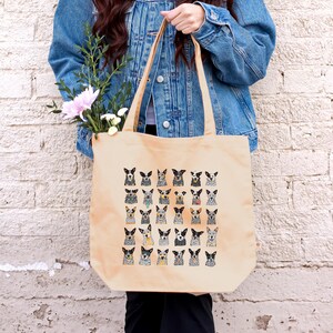 May include: A beige canvas tote bag with a pattern of cartoon Australian Shepherd dogs. The dogs are all different colors and have different expressions.