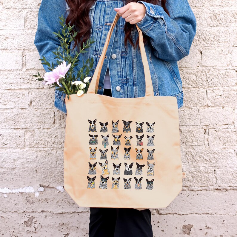 May include: A beige canvas tote bag with a pattern of cartoon Australian Shepherd dogs. The dogs are all different colors and have different expressions.