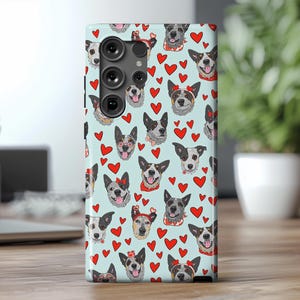 May include: A blue phone case with a pattern of Australian Shepherd dogs and red hearts. The case has a camera cutout and a raised lip around the edges.