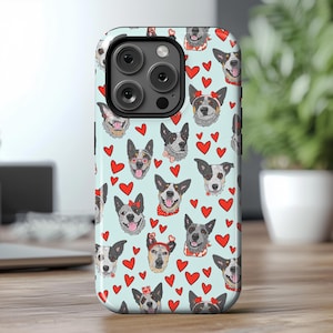 May include: A blue and white phone case with a pattern of hearts and Australian Shepherd dogs. The case has a cutout for the camera lens.