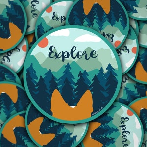 May include: A round sticker with a teal border and a forest scene with mountains in the background. The text "Explore" is written in white cursive font. The sticker has a silhouette of a dog's head in the foreground.