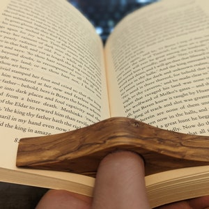 May include: A close-up of a wooden book holder, with a natural wood grain finish, holding open a book. The book is open to a page with text about a mythical creature.