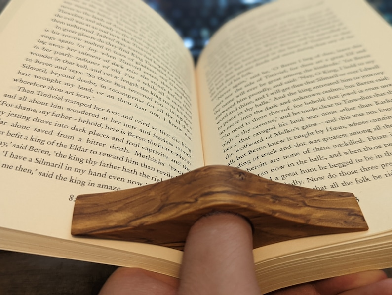 May include: A close-up of a wooden book holder, with a natural wood grain finish, holding open a book. The book is open to a page with text about a mythical creature.