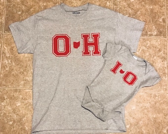 May include: A gray t-shirt with the letters "O-H" in red with an outline of the state of Ohio in between the letters. A smaller gray onesie with the letters "I-O" in red with an outline of the state of Ohio in between the letters.