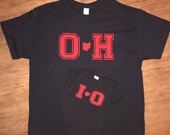 May include: Two black t-shirts with red lettering. The larger shirt says "O-H" with an outline of the state of Ohio between the letters. The smaller shirt says "I-O" with an outline of the state of Ohio between the letters.