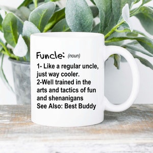 May include: White ceramic mug with the definition of "Funcle" printed in black. The definition describes a fun uncle. The mug is displayed with green leafy plants in the background.