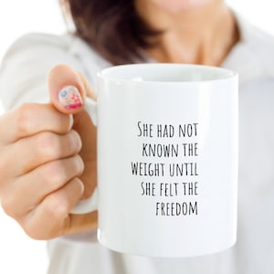 May include: White ceramic mug with black text that reads "She had not known the weight until she felt the freedom".