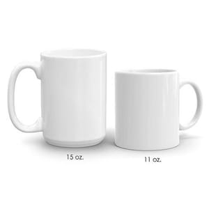 May include: Two white ceramic mugs, one labelled "15 oz." and the other "11 oz." Both mugs have a simple, cylindrical design with a curved handle. The mugs are set against a plain white background.