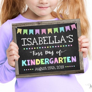 May include: A chalkboard sign with a wooden frame held by a young girl. The sign reads "ISABELLA'S First Day of KINDERGARTEN August 25th, 2019" with colorful banner and dot decorations. The text "EDIT, DOWNLOAD AND PRINT NOW" is also visible.