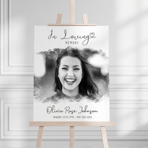 Pode incluir: Uma placa memorial em preto e branco em um cavalete de madeira. A placa apresenta um retrato de uma mulher sorrindo, as palavras "In Loving Memory" e o nome "Olivia Rose Johnson" com datas de nascimento e falecimento.