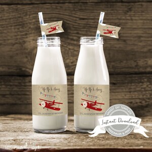 May include: Two clear glass milk bottles with red and blue airplane themed labels. The labels say "Up Up & Away" and "It's Jackson's 1st Birthday".