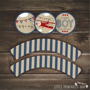 May include: Printable cupcake wrappers with blue and beige stripes. Three round cupcake toppers with a red airplane, blue and red bunting, and the text "A Baby Boy Is On The Way!"