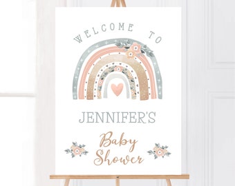 Puede incluir: Un letrero de bienvenida para baby shower sobre un caballete. El letrero presenta un arcoíris de acuarela en colores pastel, con el texto "Bienvenida a la baby shower de Jennifer". Acentos florales y un corazón completan el diseño.