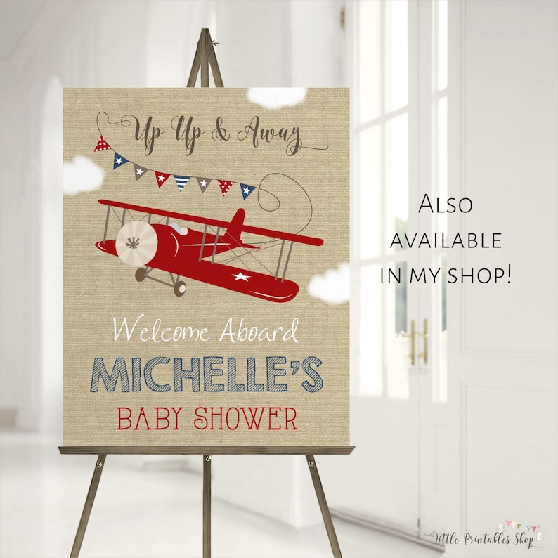 May include: A burlap baby shower welcome sign with a red airplane, blue and white bunting, and the text "Up Up & Away", "Welcome Aboard", "Michelle's Baby Shower".