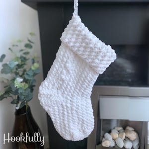 May include: White crocheted Christmas stocking hanging from a fireplace mantel. The stocking has a fluffy texture and a turned-up cuff.