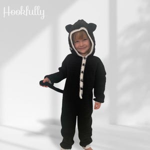 May include: A black crocheted baby costume with a white trim and a cat hood. The costume has a button closure and a tail.