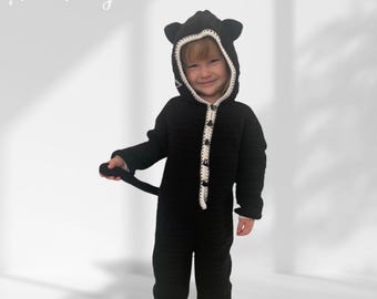 May include: A black crocheted baby costume with a white trim and a cat hood. The costume has a button closure and a tail.