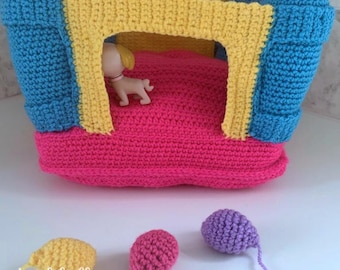 May include: A crocheted playset for dolls, featuring a pink and blue bouncy house with a yellow archway. Three small crocheted balls are included in purple, pink, and yellow.
