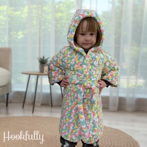May include: A colorful hooded robe with a tie belt. The robe is made of a soft, fluffy yarn in shades of pink, yellow, green, and white.