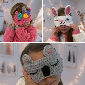 Op de afbeelding: Drie gehaakte slaapmaskers met dierenontwerpen. Het eerste masker is roze met een eenhoornontwerp. Het tweede masker is wit met een konijnenontwerp. Het derde masker is grijs met een koalaontwerp.