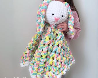May include: A white crocheted bunny with pastel pink, yellow, and green ears and body. The bunny is a baby blanket with a crocheted texture.