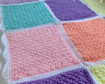 May include: A colourful crochet baby blanket with a white border. The blanket is made up of squares in different pastel colours, including pink, purple, blue, orange, and yellow. The text "Hookfully" is visible in the top right corner of the blanket.