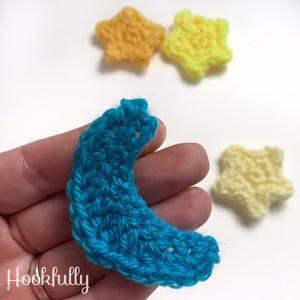 May include: A crocheted blue crescent moon shape, with three crocheted yellow stars in the background.