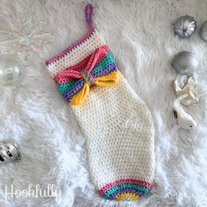 May include: A white crocheted Christmas stocking with a multi-colored striped bow at the top. The stocking has a pink, green, purple, and yellow stripe at the cuff.