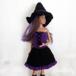 Puede incluir: Un disfraz de bruja de ganchillo para una muñeca, que incluye un sombrero negro con una banda morada, un corpiño morado y una falda negra con un ribete morado.