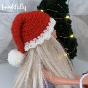 Op de afbeelding: Een rood-witte gehaakte kerstmanmuts met een witte pompon. De muts zit op een pop met lang blond haar.