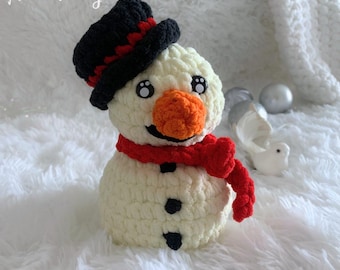May include: A crocheted snowman with a black top hat, red scarf, and orange nose. The snowman is white with black eyes and buttons.