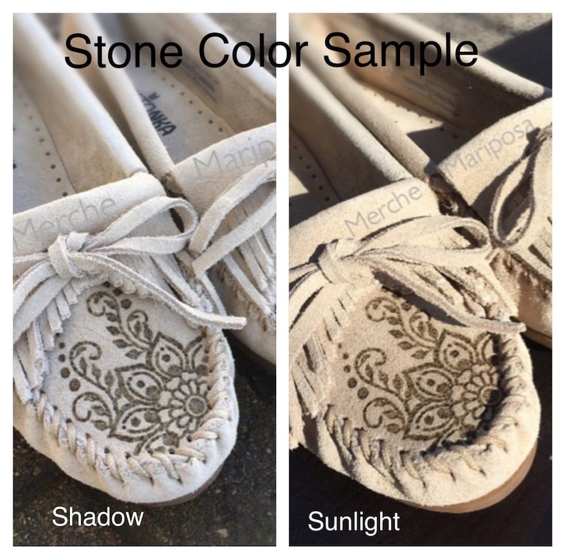 May include: Close-up of a pair of beige suede moccasins with fringe and a decorative pattern. The image shows the shoes in both shadow and sunlight to illustrate the color variation.
