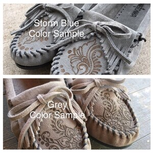 May include: Two pairs of moccasins, one pair in grey and one pair in storm blue. Both pairs have a decorative pattern and fringe.