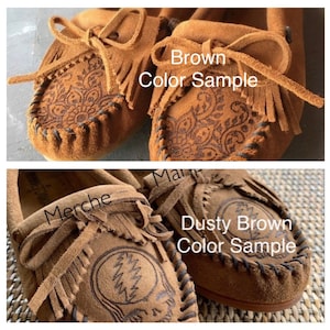 May include: Two pairs of brown suede moccasins with fringe. The moccasins on the top are labeled "Brown Color Sample" and the moccasins on the bottom are labeled "Dusty Brown Color Sample".