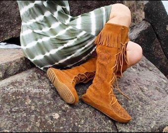 May include: Brown leather knee-high boots with fringe and intricate floral embroidery. The boots are laced up the front and have a pointed toe.