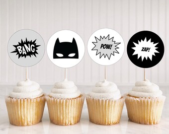 May include: Four black and white cupcake toppers with superhero themes. The toppers feature a batman mask, "POW!" "ZAP!" and "BANG!" text.