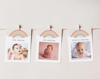 May include: Three baby milestone cards hanging on a string. Each card features a photo of a baby and a rainbow design. The cards are labeled "ONE MONTH", "SIX MONTHS", and "TWELVE MONTHS".