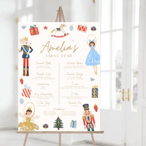 May include: A white printable poster with a gold and white title "Amelia's First Year". The poster features illustrations of a nutcracker, a ballerina, a rocking horse, and Christmas ornaments. The poster includes a list of Amelia's first year milestones, including favorite foods, songs, books, and toys.
