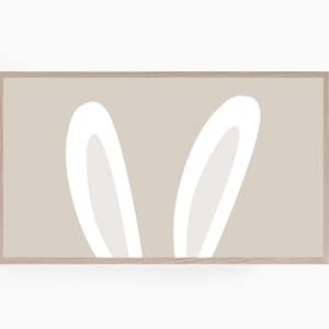 Può includere: Una stampa incorniciata con uno sfondo beige e due orecchie di coniglio bianche. Le orecchie sono stilizzate e hanno un design semplice e moderno.