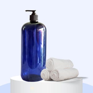 May include: A blue plastic pump bottle with a black pump top, sitting on a white surface next to three white rolled-up towels.