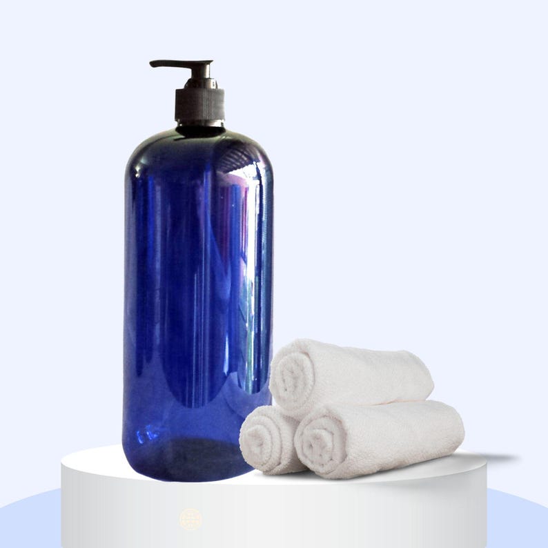 May include: A blue plastic pump bottle with a black pump top, sitting on a white surface next to three white rolled-up towels.