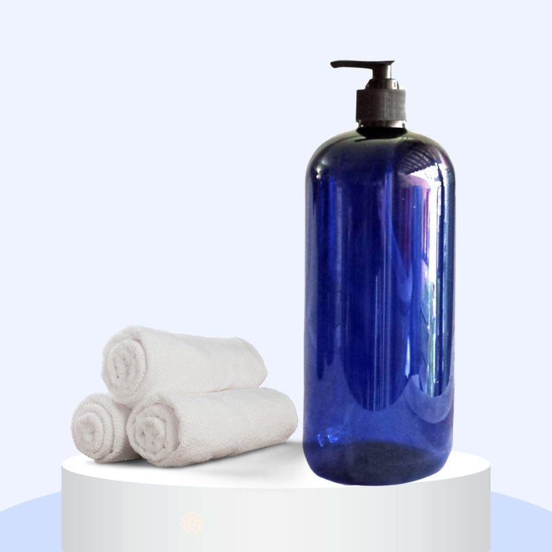 May include: A blue plastic pump bottle with a black pump top. The bottle is sitting on a white surface next to three white rolled up towels.