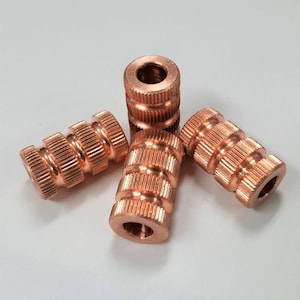 May include: Four copper-colored threaded inserts with a ridged design. The inserts are arranged in a star shape.